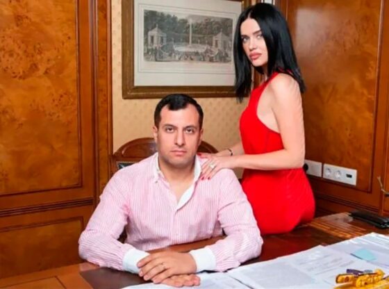 Boris Avakyan, 43, in a striped shirt, sitting at a wooden desk with his wife Julia, in a red dress, leaning on his shoulder.