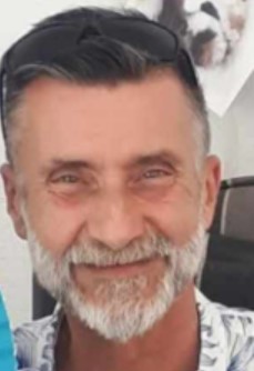 A man with a gray beard and sunglasses on his head smiling slightly.