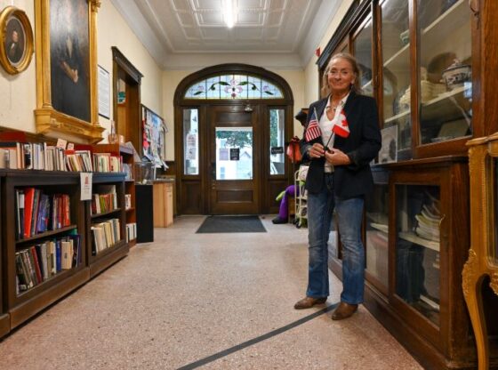Sylvie Boudreau, president of the board of trustees of the cross-border Haskell Library, poses for a picture standing on the black marker that indicates the US (L) and Canada sides, inside the library in Stanstead, Quebec, Canada, on October 22, 2025.