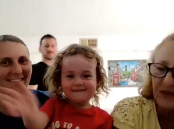 A woman in a blue shirt waving, a child in a red shirt smiling, a man, and a woman in glasses.