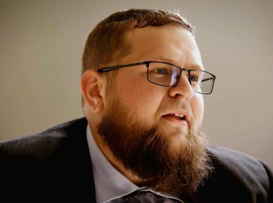 A man with a beard and glasses looking to the right.