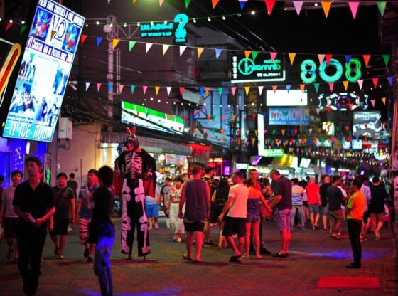 People walking down Walking Street in Pattaya, Thailand at night, with neon lights and colorful pennants strung above.