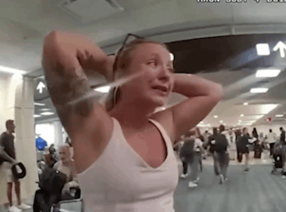 A woman with her hands on her head, crying, while others walk in an airport terminal.