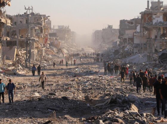 Dozens of Palestinians walk through the rubble of a Gaza City street.
