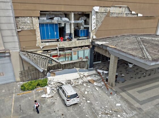 A security guard walks past a damaged wall and a car outside a mall in Butuan City after a 7.4-magnitude earthquake.