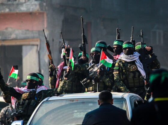 Hamas militants on a car in Jabalia ahead of a hostage exchange, displaying weapons and Palestinian flags.